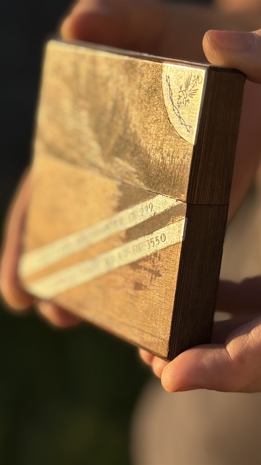 Zbigniew's cigarette box, made in the camp at Aslau — the crowned white-eagle emblem in the corner and his prisoner numbers worked into the metal, held to the light